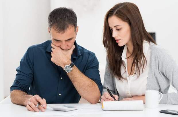 man and woman at table with calculator and papers; woman is taking notes