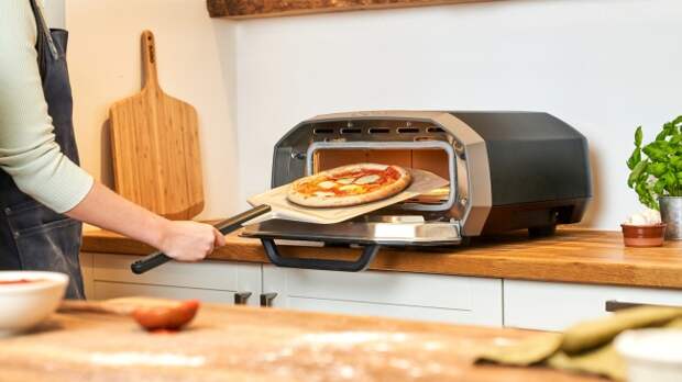 The Ooni Volt 12 electric pizza oven in a kitchen setting, with a pizza being put in the oven