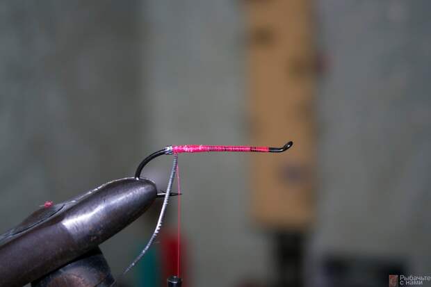 Зафиксируйте монтажную нить на цевье крючка, после чего закрепите люрекс и сделайте два витка возле загиба крючка.