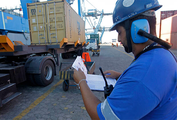 Рабочий регистрирует погрузку контейнера на грузовое судно 