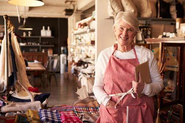 A person wearing an apron standing next to shelves of apparel in a store.