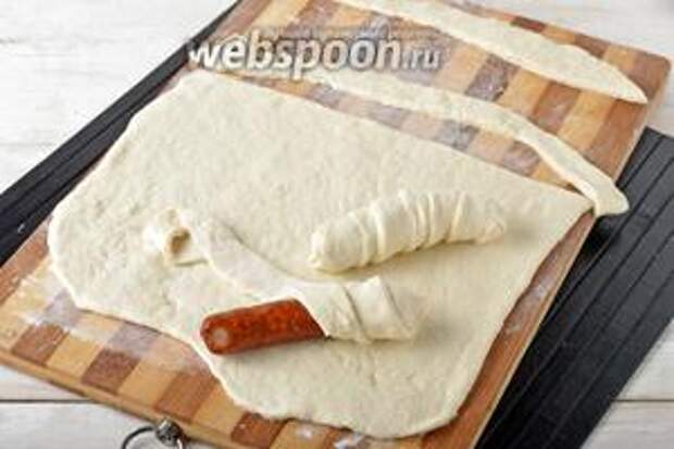 Раскатать тесто толщиной 2-3 миллиметра на подпылённой мукой доске. Нарезать тесто на полоски шириной 1 сантиметр. Замотать каждую сосиску в тесто, наматывая тесто по спирали.
