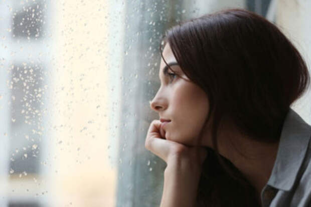 Одинокая женщина смотрит в окно. На улице идет дождь