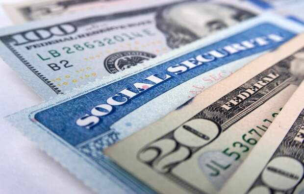 A Social Security card wedged into a fan of U.S. paper currency of varying denominations.