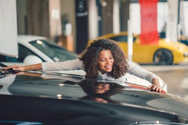 Happy person hugging car at a dealer lot.