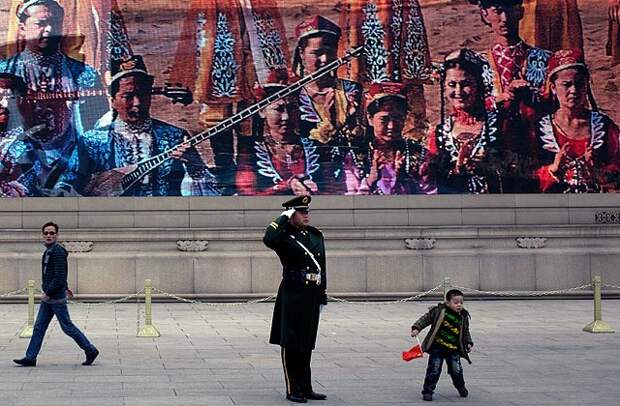 Китайский полицейский на фоне изображения уйгуров. Фото: Andy Wong / AP
