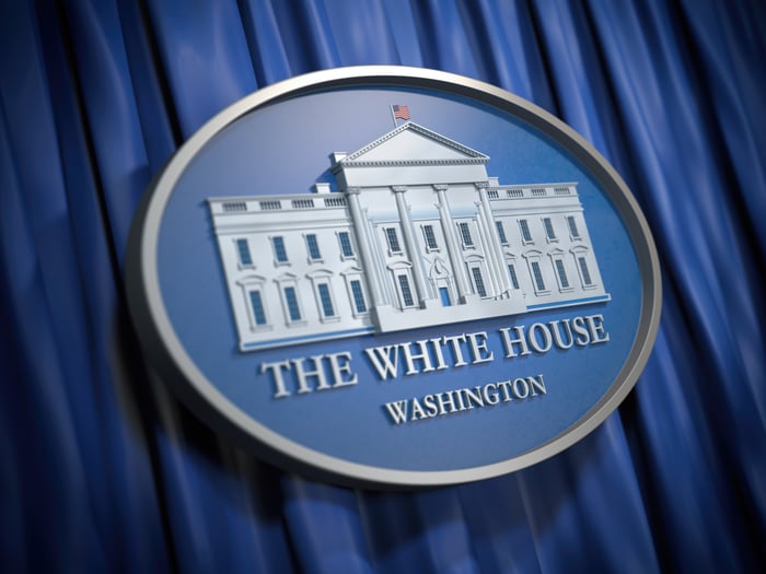 The White House logo in front of a blue curtain.