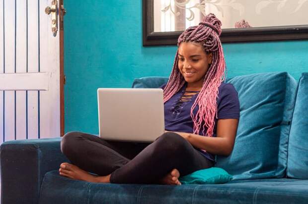 Smiling person sitting cross-legged on couch using laptop.