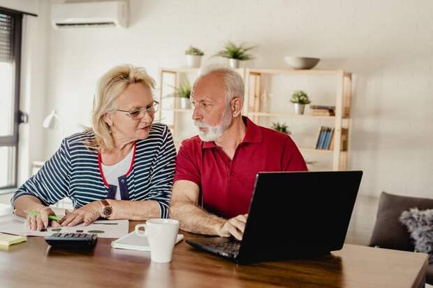 Two seniors sitting at a table with a laptop and calculator.