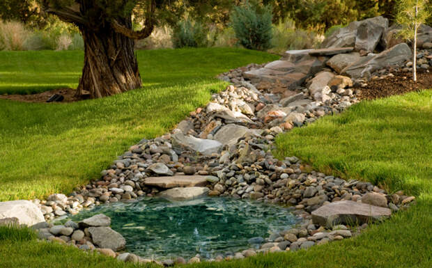 Маленький пруд с небольшим фонтаном. Густая трава и различные фигурки украшают каменные берега водоёма.