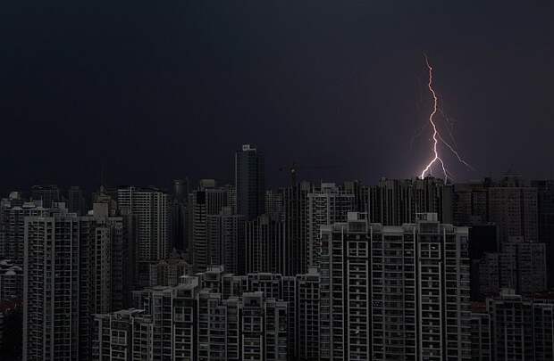 Удар молнии над темными зданиями в центре Шанхая во время шторма 15 августа 2012