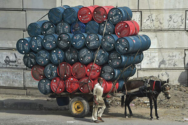 Мужчина рядом с повозкой груженной бочками с нефтью на  улице в Лахоре 
