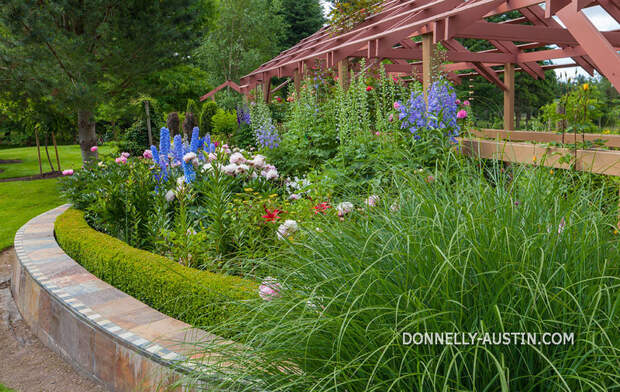 Vashon Island, WA: Curved flower bed with rose pergola with colorful blooms of peonies and delphiniums in Froggsong garden in summer