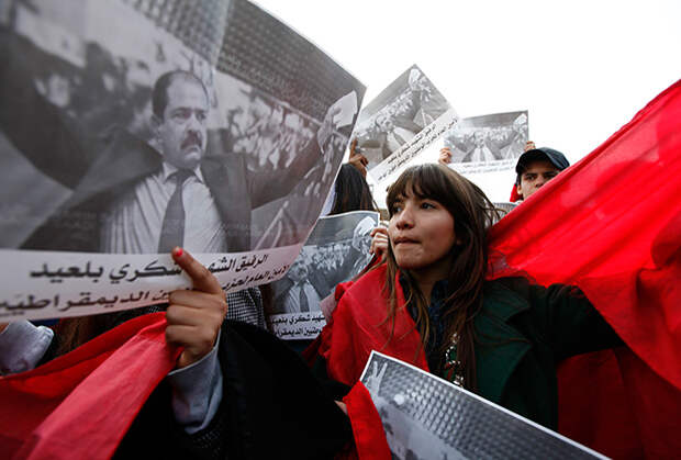 Женщина стоит около фотографии Шокри Белаида во время протестов 2013 года