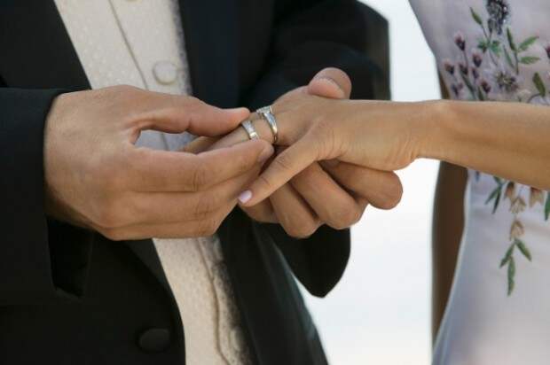 Мужчина надевает женщине кольцо на палец рядом с помолвочным