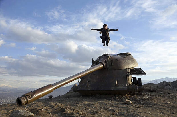 Афганский мальчик прыгает с башни советского танка на вершине холма на окраине Кабула