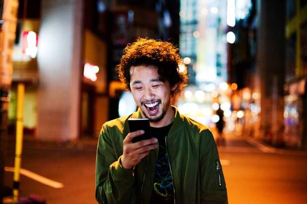 Smiling person looking at smartphone on city street.