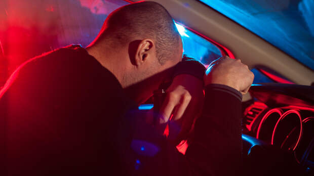 Upset drunk driver is caught driving under alcohol influence. Man covering his face from police car light.