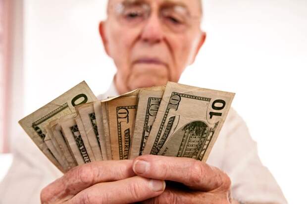 A person counting an assorted pile of fanned cash bills in their hands.
