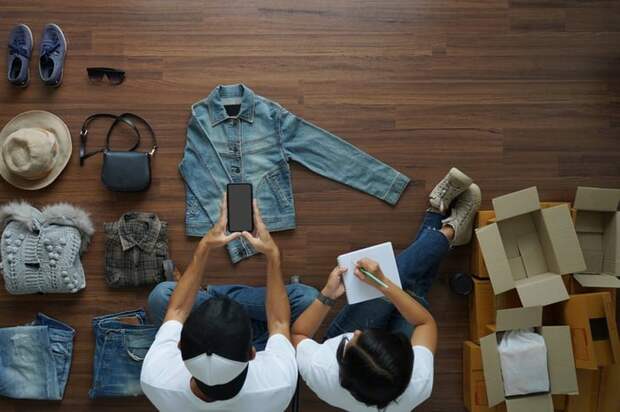 Two people sitting on the floor and taking pictures of their used clothes to sell.