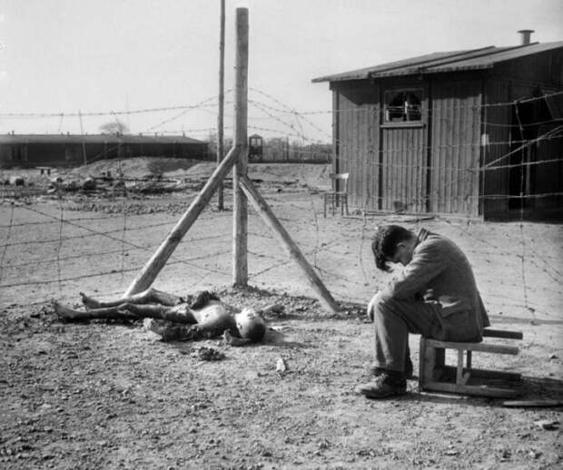 Молодой человек сидит на перевернутом табурете рядом с сожженным телом в лагере Фекла.