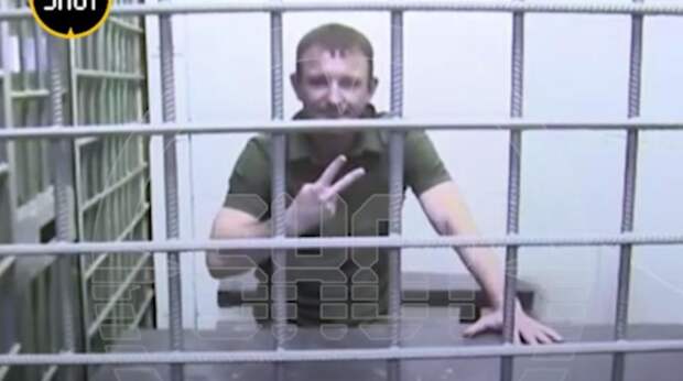 Генерал Попов показал пальцами знак V через клетку во время суда