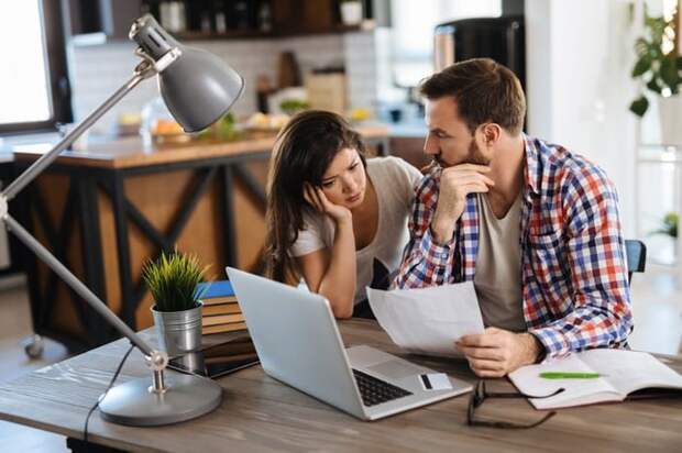 Frustrated young couple checks their bills at home using a laptop.